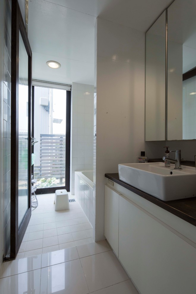 Example of a white tile and porcelain tile ceramic tile and white floor bathroom design in Other with a two-piece toilet, white walls, a vessel sink, wood countertops, a hinged shower door and brown countertops