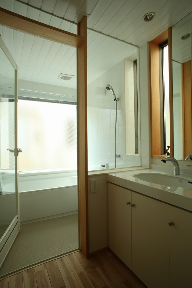 На фото: главная ванная комната среднего размера со стиральной машиной в стиле модернизм с белыми стенами, бежевым полом, фасадами с декоративным кантом, белыми фасадами, белой плиткой, керамогранитной плиткой, паркетным полом среднего тона, врезной раковиной, столешницей из искусственного камня, белой столешницей, напольной тумбой, японской ванной, душевой комнатой, душем с распашными дверями и тумбой под одну раковину с