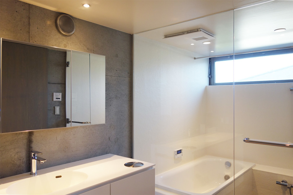 Aménagement d'une salle de bain moderne avec des portes de placard blanches, un bain japonais, un espace douche bain, un carrelage rose, un mur gris, un lavabo intégré, un plan de toilette en surface solide, aucune cabine et un plan de toilette blanc.