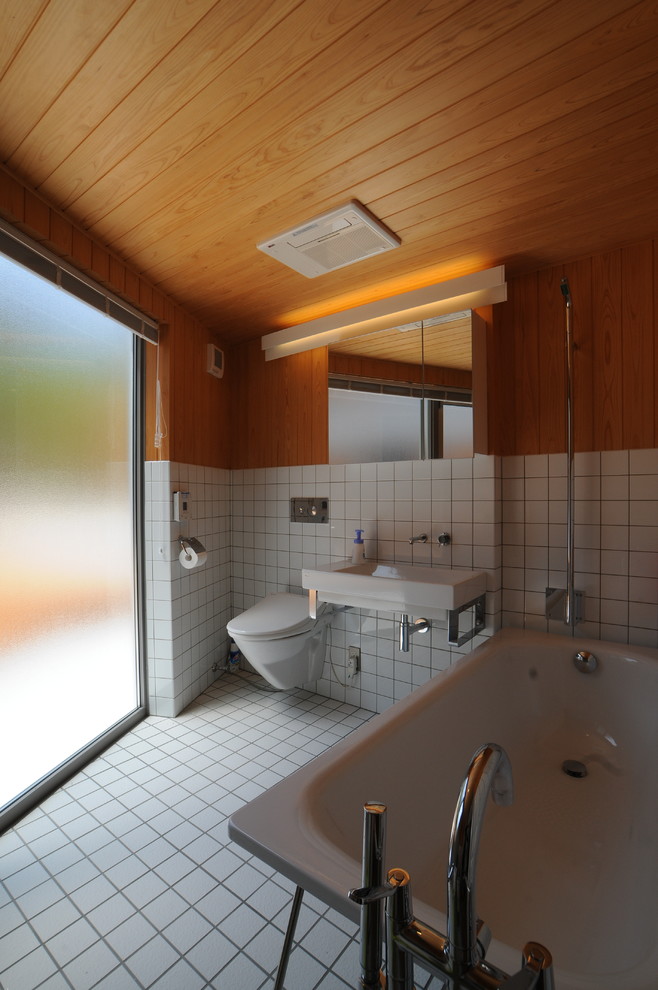 Example of a trendy white tile freestanding bathtub design in Other with a wall-mount toilet, white walls and a wall-mount sink