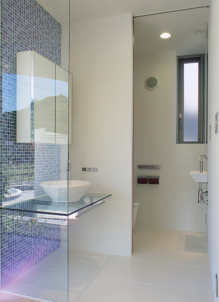 他の地域にあるコンテンポラリースタイルのおしゃれな浴室 (青いタイル、ベッセル式洗面器、ガラスの洗面台、白い床) の写真