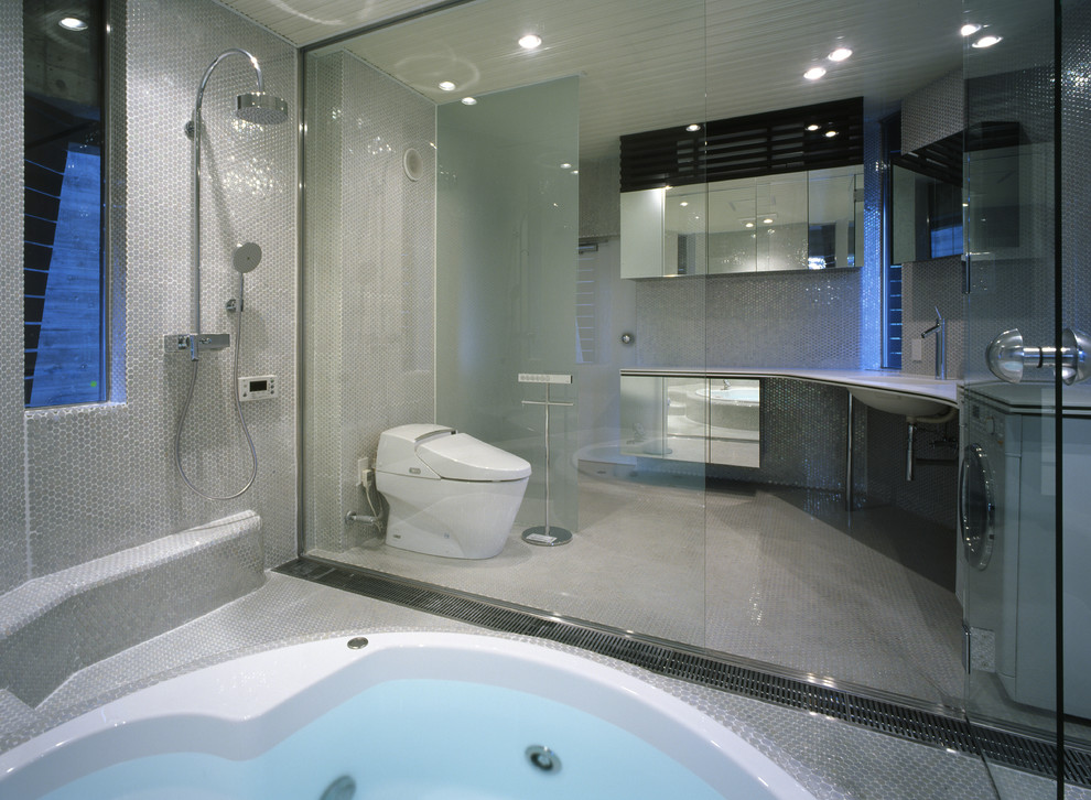Foto di una stanza da bagno design con ante lisce, vasca sottopiano, doccia a filo pavimento, WC sospeso, piastrelle grigie e pareti grigie