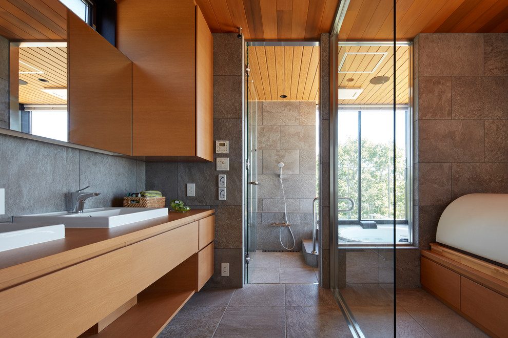 他の地域にあるアジアンスタイルのおしゃれな浴室 (フラットパネル扉のキャビネット、中間色木目調キャビネット、グレーのタイル、グレーの壁、オーバーカウンターシンク、グレーの床) の写真