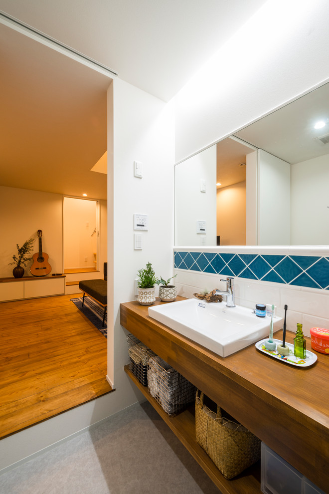 Nordisches Badezimmer mit offenen Schränken, weißer Wandfarbe, Einbauwaschbecken, Waschtisch aus Holz, grauem Boden und brauner Waschtischplatte in Sonstige