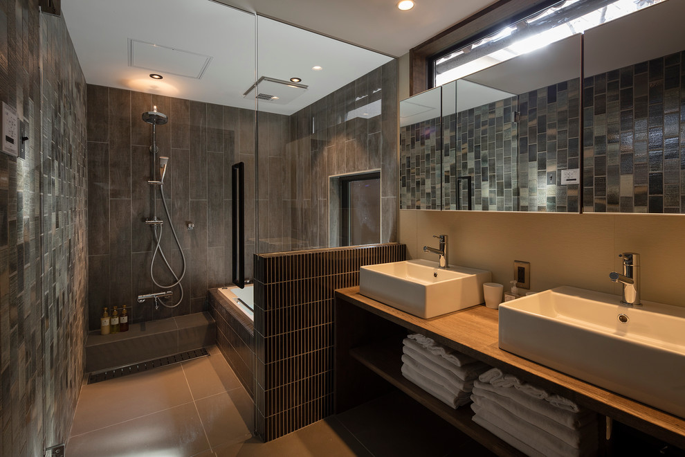 Inredning av ett modernt badrum, med öppna hyllor, ett platsbyggt badkar, grå kakel, grå väggar, ett fristående handfat och med dusch som är öppen