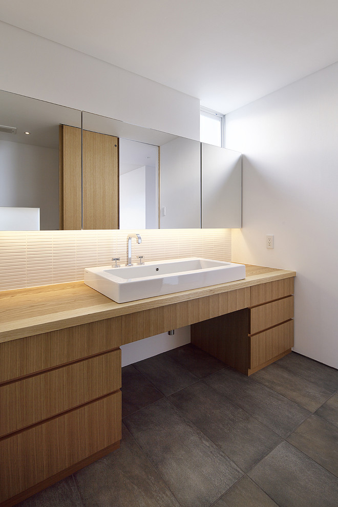 На фото: ванная комната в стиле модернизм с плоскими фасадами, светлыми деревянными фасадами, белой плиткой, белыми стенами, бетонным полом, настольной раковиной, столешницей из дерева и коричневой столешницей