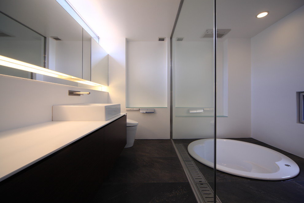 Diseño de cuarto de baño minimalista con armarios con paneles lisos, jacuzzi, sanitario de una pieza, paredes blancas, lavabo sobreencimera, puertas de armario marrones, baldosas y/o azulejos grises y suelo gris