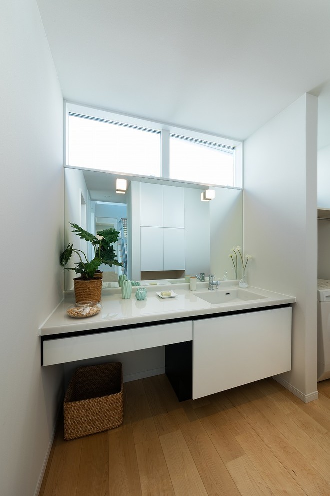 Immagine di una stanza da bagno design con ante lisce, ante bianche, pareti bianche, pavimento in legno massello medio, lavabo integrato e pavimento marrone