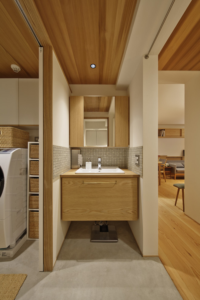 This is an example of a world-inspired bathroom in Kyoto with flat-panel cabinets, medium wood cabinets, white walls, concrete flooring, a built-in sink and grey floors.