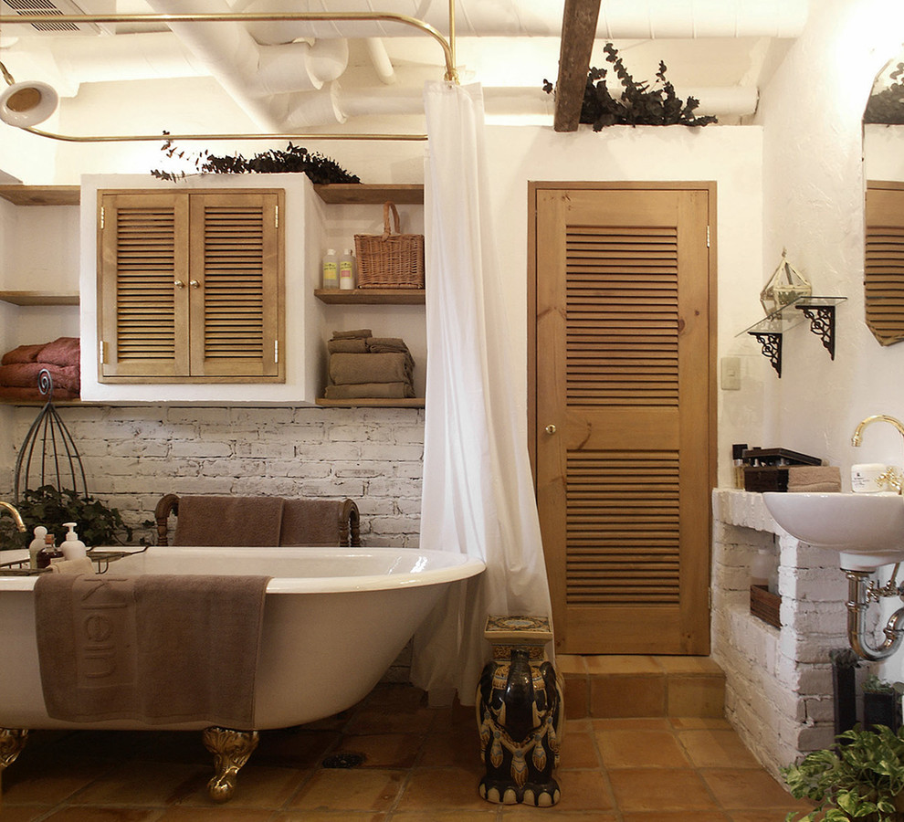 Bild på ett lantligt badrum, med ett badkar med tassar, vita väggar, klinkergolv i terrakotta, ett konsol handfat och brunt golv