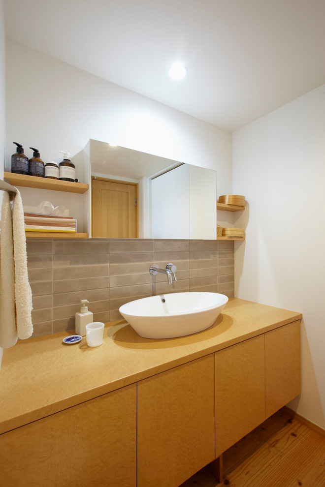 Exempel på ett modernt brun brunt badrum, med släta luckor, bruna skåp, grå kakel, vita väggar, mellanmörkt trägolv, ett fristående handfat, träbänkskiva och brunt golv