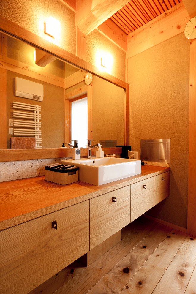 Example of an asian medium tone wood floor and brown floor bathroom design in Other with flat-panel cabinets, medium tone wood cabinets, brown walls, a vessel sink, wood countertops and brown countertops