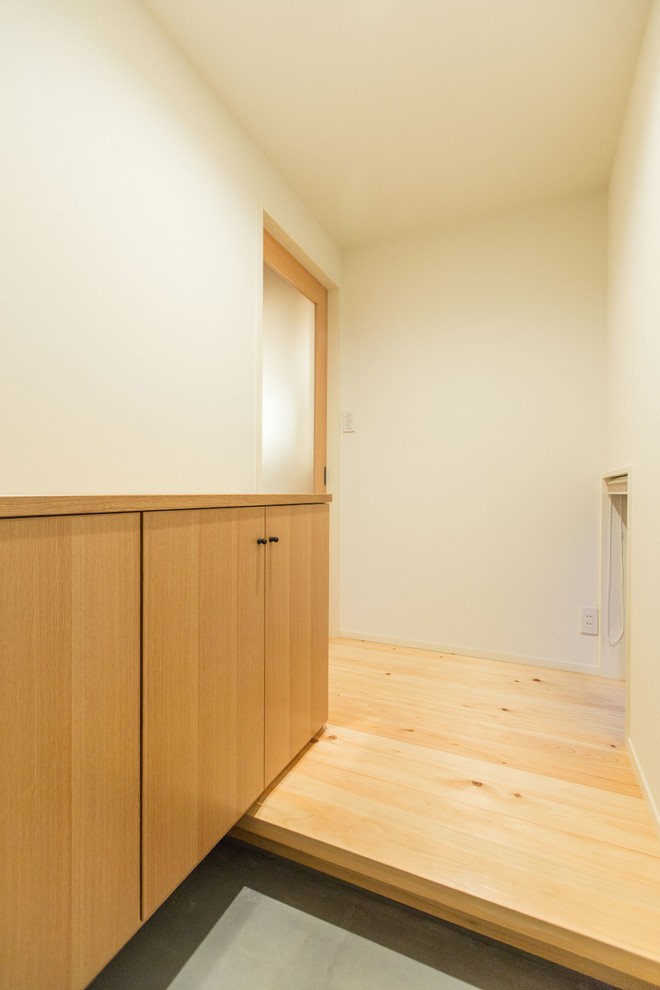 Cette image montre une petite entrée asiatique avec un couloir, un mur blanc, parquet clair, une porte simple, une porte grise et un sol beige.