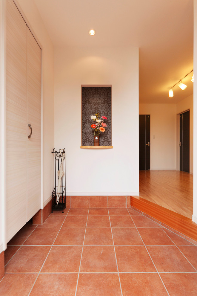 他の地域にある広いカントリー風のおしゃれな玄関ホール (白い壁、テラコッタタイルの床、木目調のドア、茶色い床) の写真