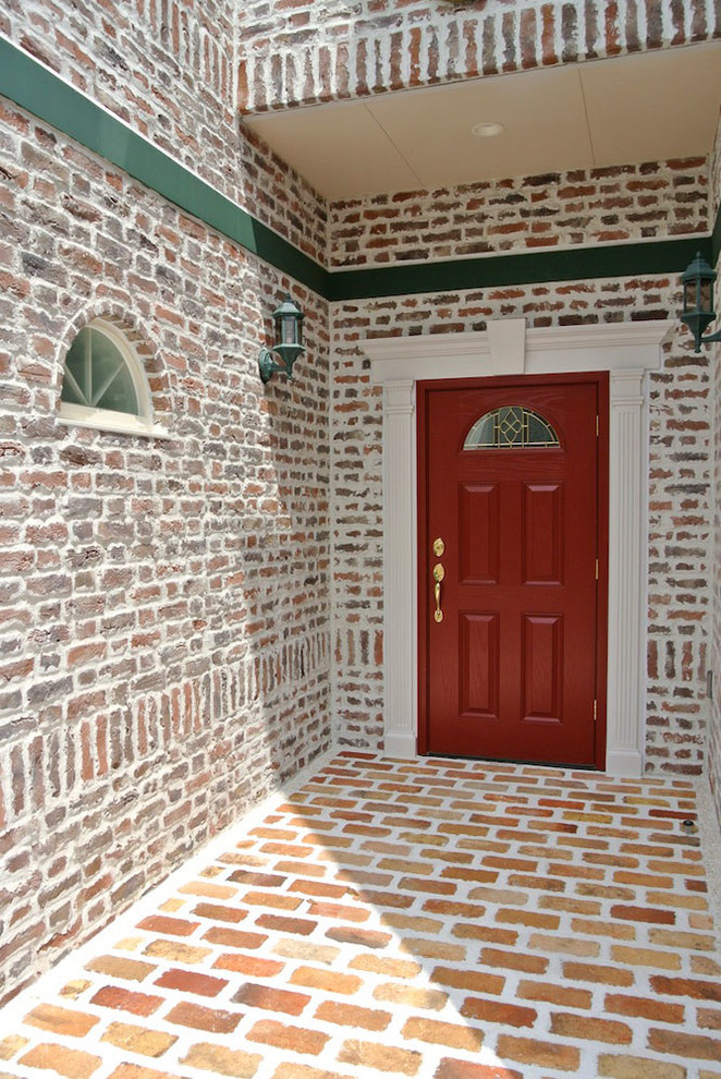 Inredning av en klassisk stor ingång och ytterdörr, med rosa väggar, tegelgolv, en röd dörr och orange golv