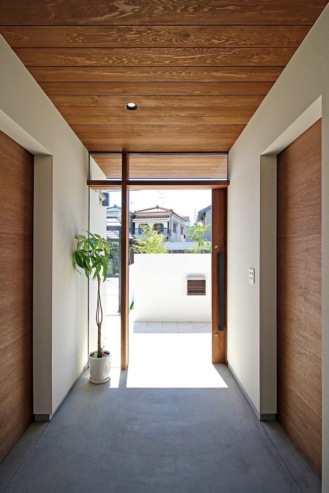 Идея дизайна: узкая прихожая в стиле модернизм с белыми стенами, бетонным полом, раздвижной входной дверью, входной дверью из дерева среднего тона и серым полом