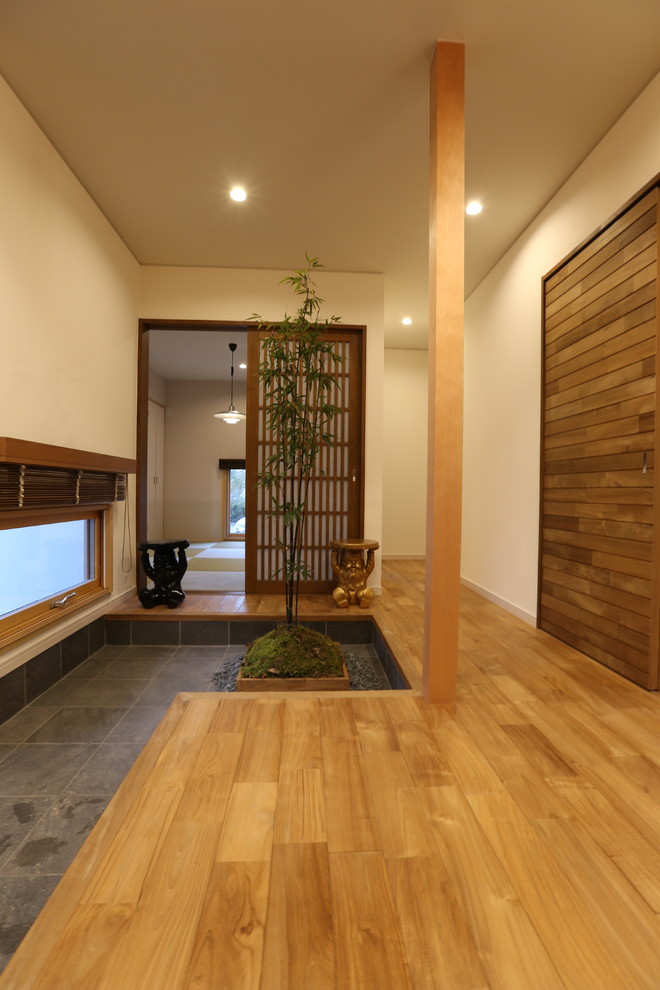Cette image montre une entrée asiatique avec un couloir, un mur blanc, parquet foncé, une porte simple et une porte marron.