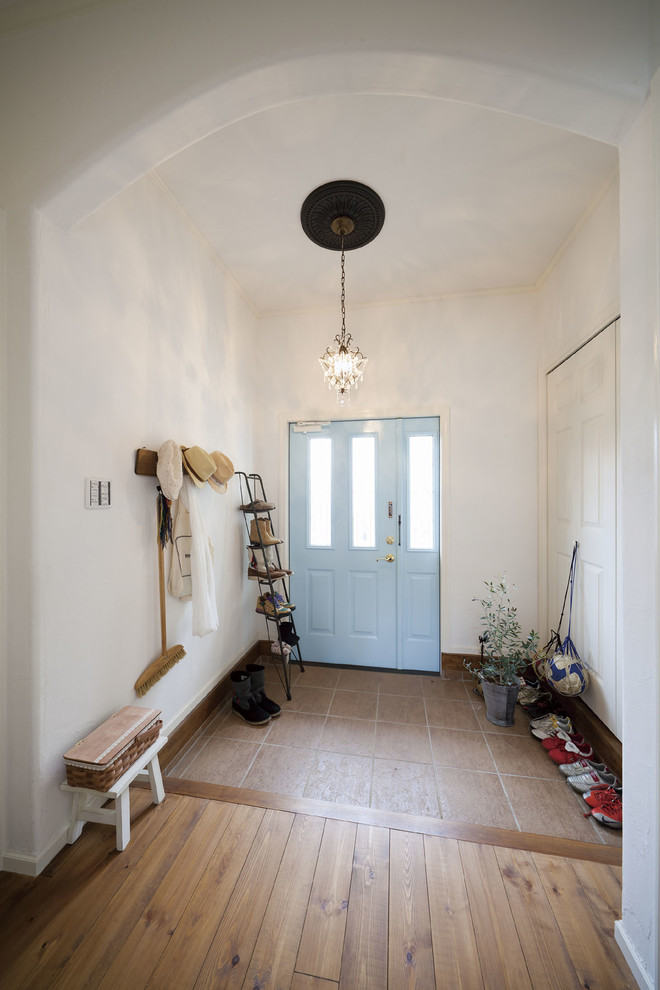 На фото: узкая прихожая в средиземноморском стиле с белыми стенами, одностворчатой входной дверью, синей входной дверью и коричневым полом с