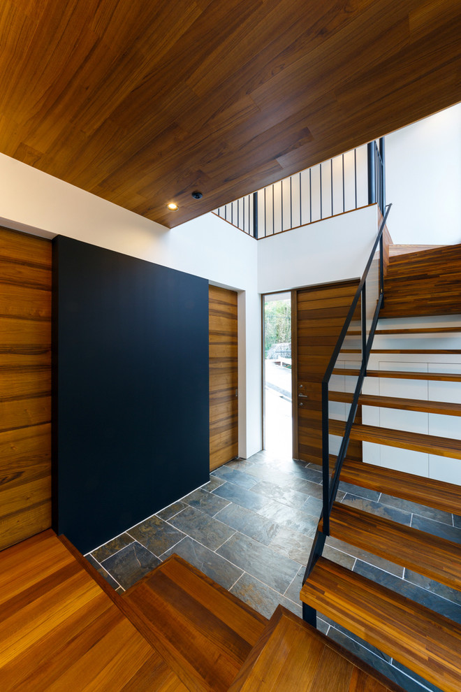 Aménagement d'une grande entrée moderne avec un couloir, un mur noir, un sol en ardoise, une porte simple, une porte marron et un sol gris.