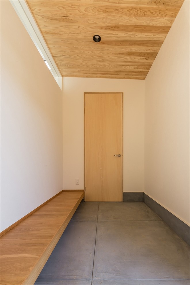 Idee per un corridoio minimalista di medie dimensioni con pareti bianche, pavimento in cemento, una porta singola, una porta in legno chiaro e pavimento grigio