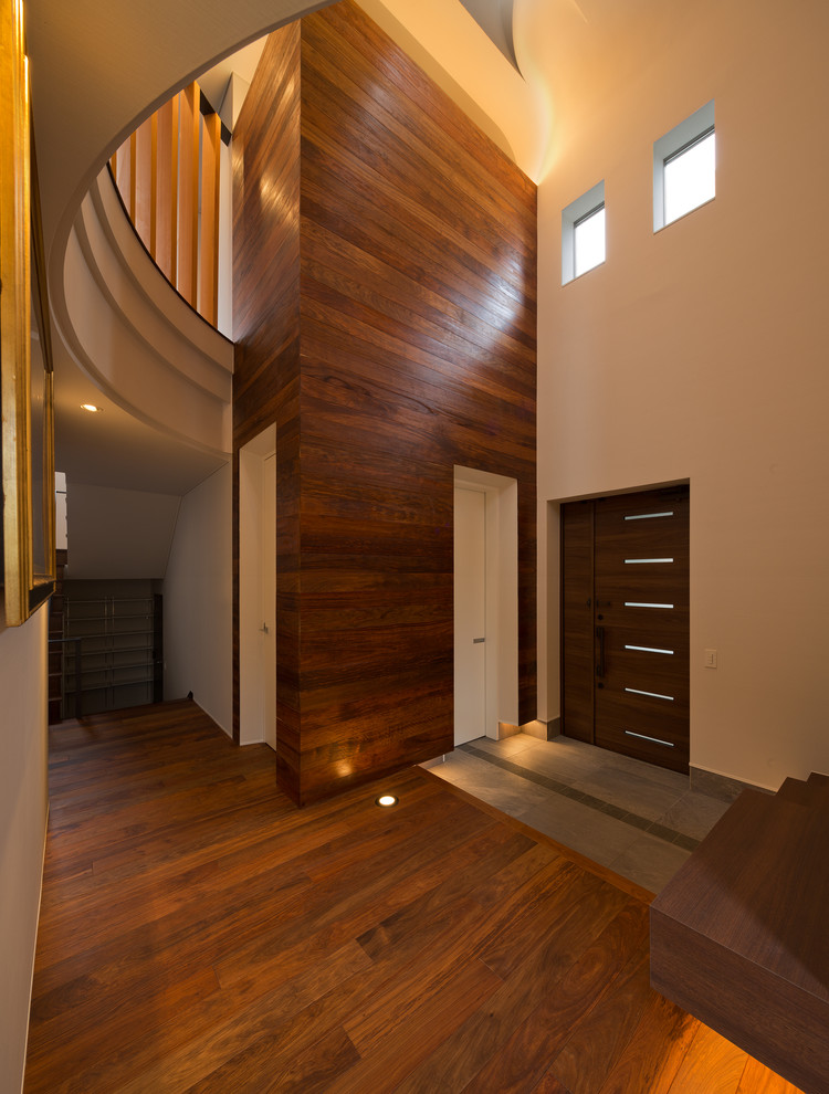 Diseño de entrada minimalista con paredes blancas, suelo de madera en tonos medios, puerta de madera oscura, puerta simple y suelo marrón