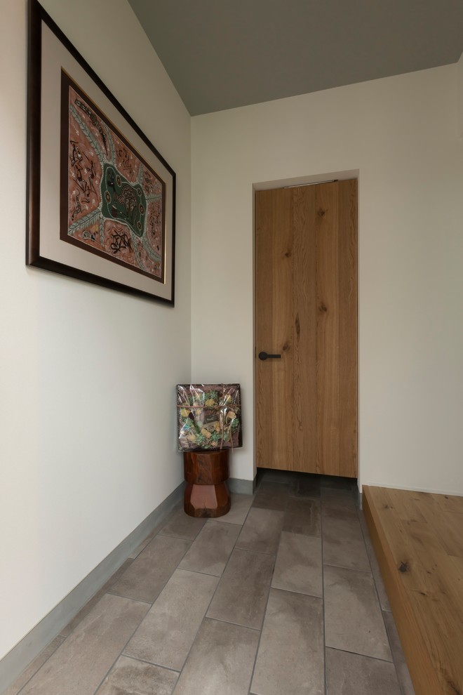 お手頃価格の中くらいなミッドセンチュリースタイルのおしゃれな玄関ホール (グレーの壁、磁器タイルの床、木目調のドア、ベージュの床) の写真