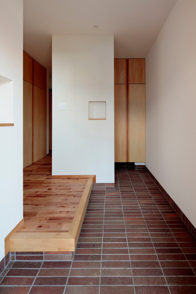 Esempio di un corridoio scandinavo di medie dimensioni con pareti bianche, pavimento in gres porcellanato, una porta singola, una porta in legno bruno e pavimento rosso
