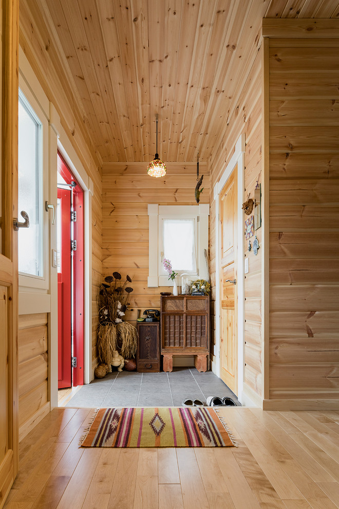 Foto på en skandinavisk entré, med bruna väggar, en enkeldörr, en röd dörr och grått golv