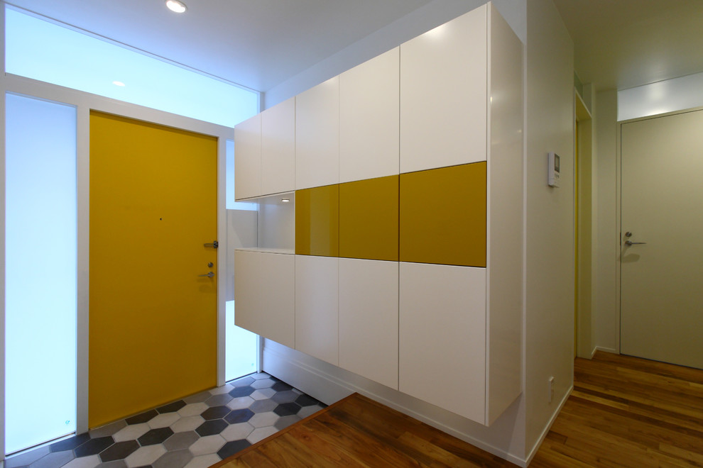 Свежая идея для дизайна: узкая прихожая среднего размера в стиле модернизм с белыми стенами, паркетным полом среднего тона, одностворчатой входной дверью, желтой входной дверью и коричневым полом - отличное фото интерьера