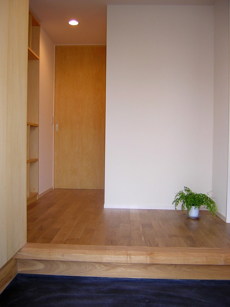 他の地域にあるお手頃価格の小さなアジアンスタイルのおしゃれな玄関ホール (白い壁、無垢フローリング、木目調のドア、茶色い床) の写真