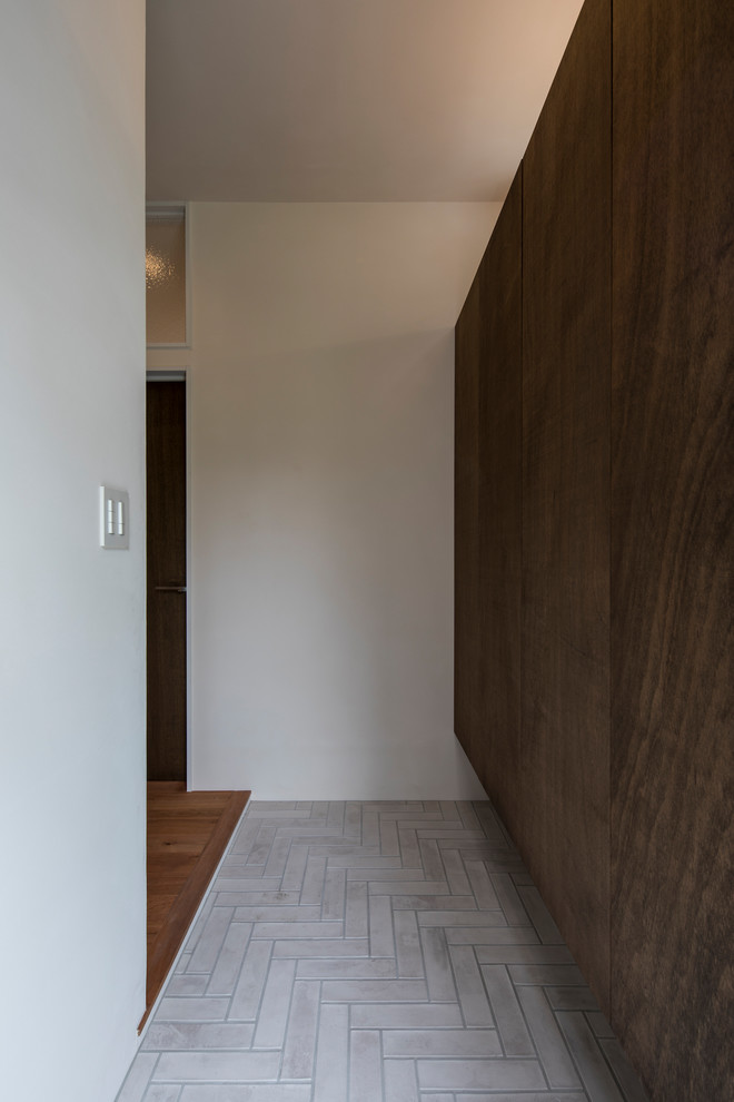 他の地域にあるコンテンポラリースタイルのおしゃれな玄関ホール (茶色い壁、磁器タイルの床、グレーの床) の写真