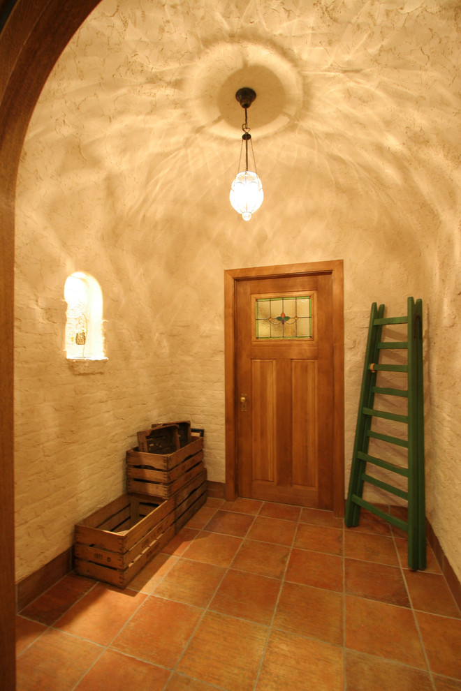 Shabby-Look Eingang mit weißer Wandfarbe, Terrakottaboden, Einzeltür, hellbrauner Holzhaustür und braunem Boden in Sonstige