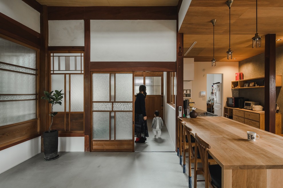 Diseño de hall asiático extra grande con paredes blancas, suelo de cemento, puerta corredera, puerta de madera en tonos medios y suelo gris