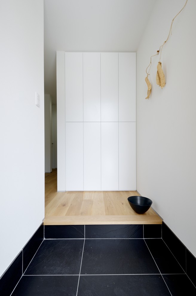 Ispirazione per un corridoio minimalista con pareti bianche, pavimento in gres porcellanato, una porta singola, una porta in legno bruno e pavimento nero