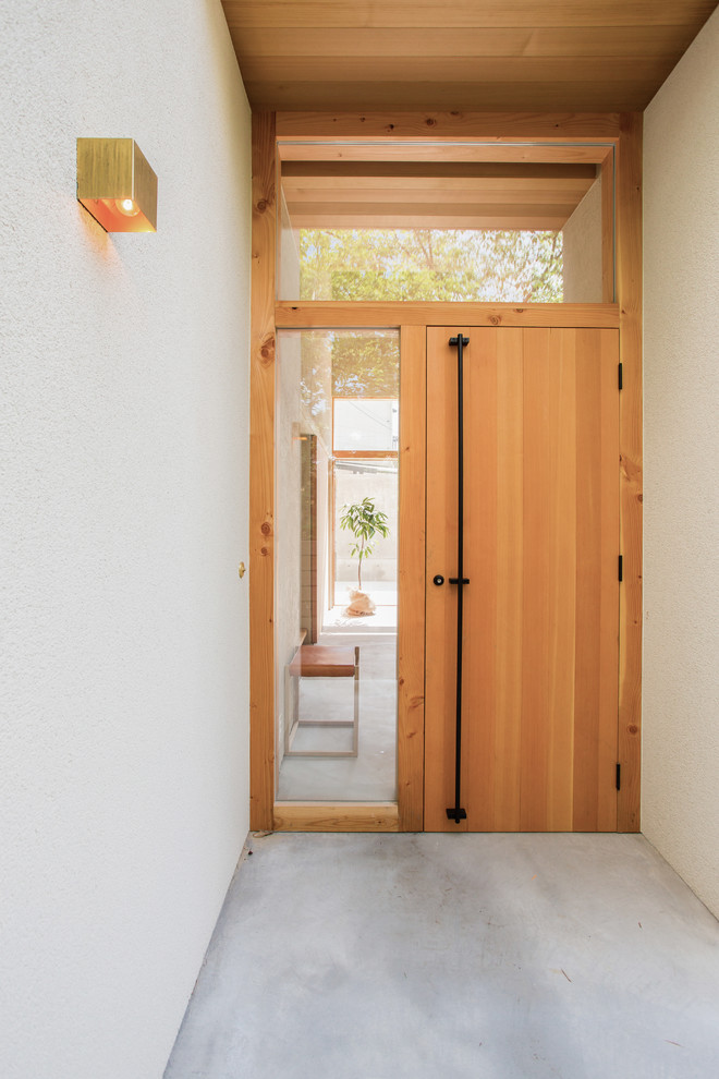 Réalisation d'une petite porte d'entrée nordique avec un mur blanc, sol en béton ciré, une porte simple, une porte en bois brun et un sol gris.