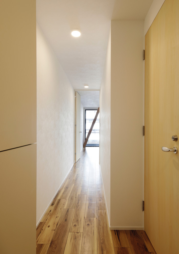 Cette image montre une petite entrée minimaliste avec un couloir, un mur blanc, un sol en linoléum, une porte simple, une porte noire et un sol beige.