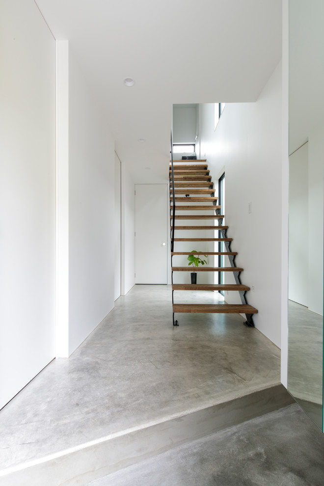 На фото: узкая прихожая в стиле модернизм с белыми стенами, бетонным полом и серым полом с