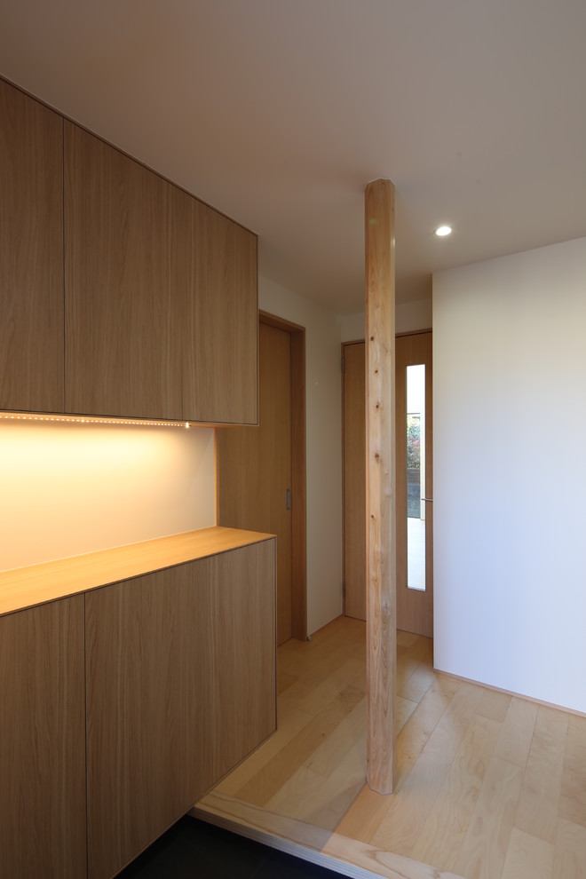 Modelo de hall minimalista pequeño con paredes blancas, suelo de madera clara, puerta corredera, puerta negra y suelo beige
