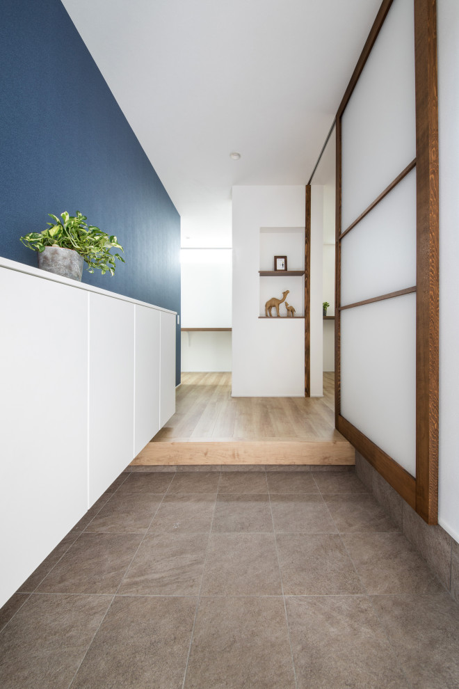 Réalisation d'une entrée minimaliste de taille moyenne avec un couloir, un mur blanc, un sol en carrelage de porcelaine, une porte coulissante, une porte en bois brun et un sol marron.