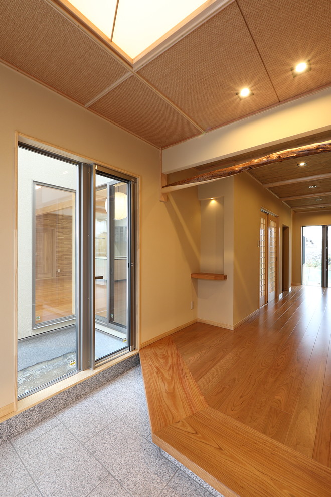 Großer Asiatischer Eingang mit Korridor, beiger Wandfarbe, Granitboden, Schiebetür, hellbrauner Holzhaustür und weißem Boden in Sonstige