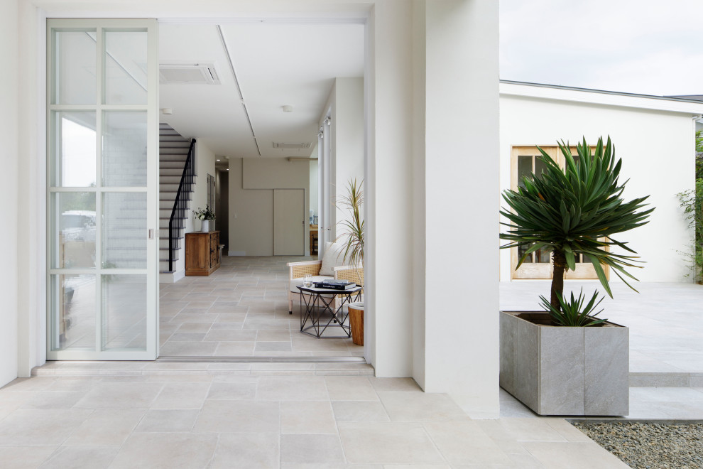 Cette photo montre une très grande entrée romantique avec un couloir, un mur blanc, un sol en carrelage de céramique, une porte coulissante, une porte en verre et un sol gris.