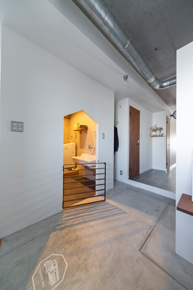 Cette image montre une petite entrée craftsman avec un couloir, un mur blanc, sol en béton ciré et un sol gris.
