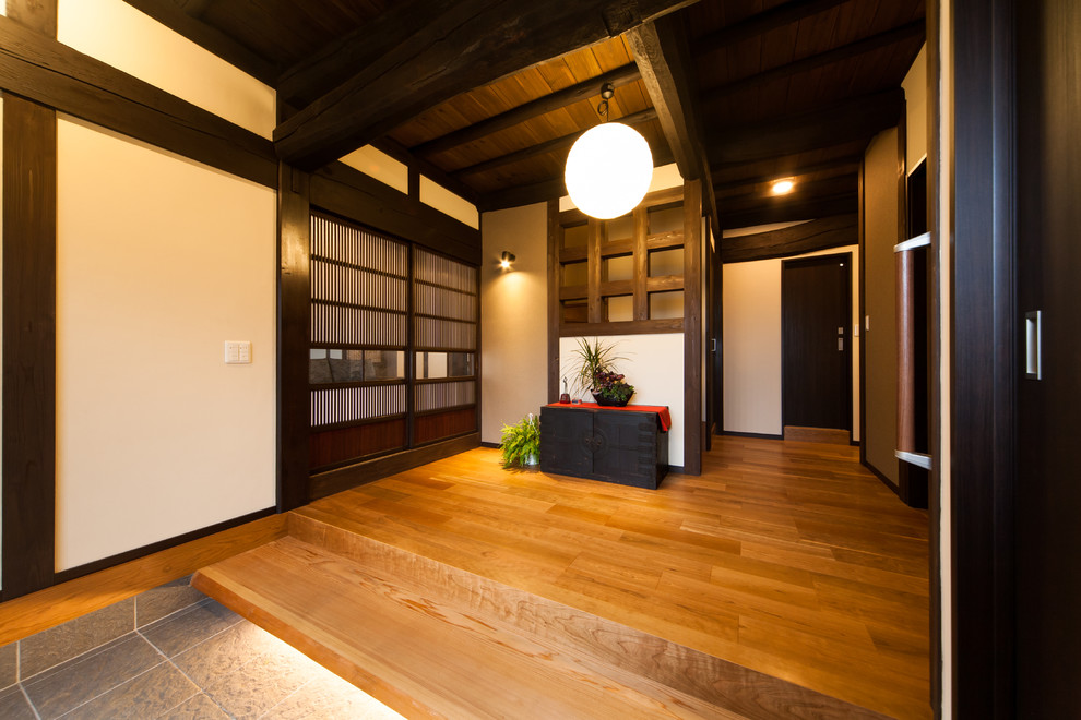 Cette image montre une entrée asiatique avec un couloir, un mur blanc, un sol en bois brun et un sol marron.