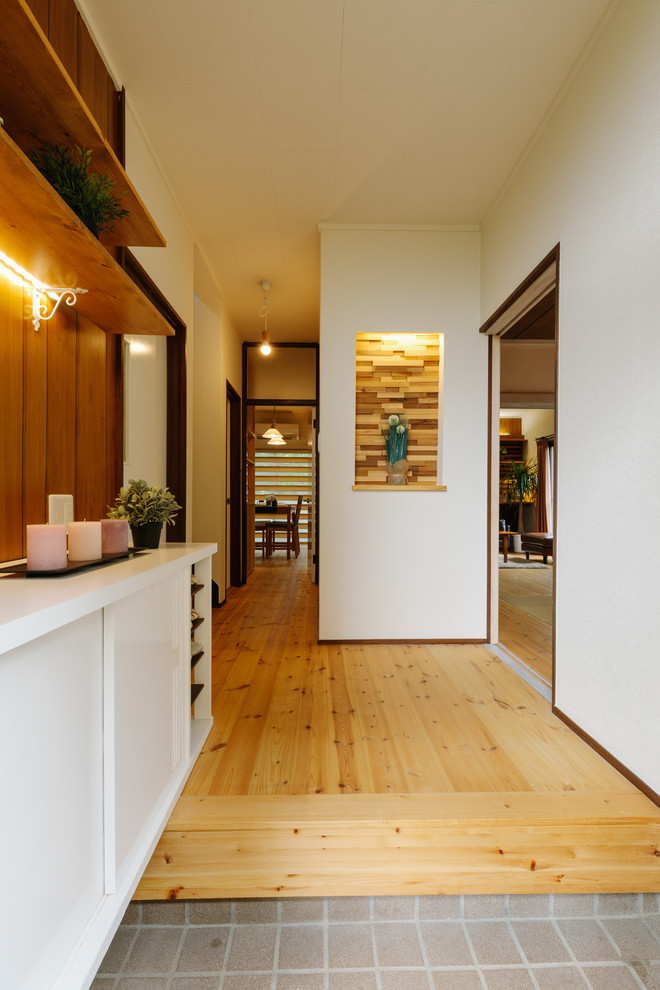 Kleiner Asiatischer Eingang mit Korridor, weißer Wandfarbe, braunem Holzboden, Einzeltür, dunkler Holzhaustür und braunem Boden in Sonstige