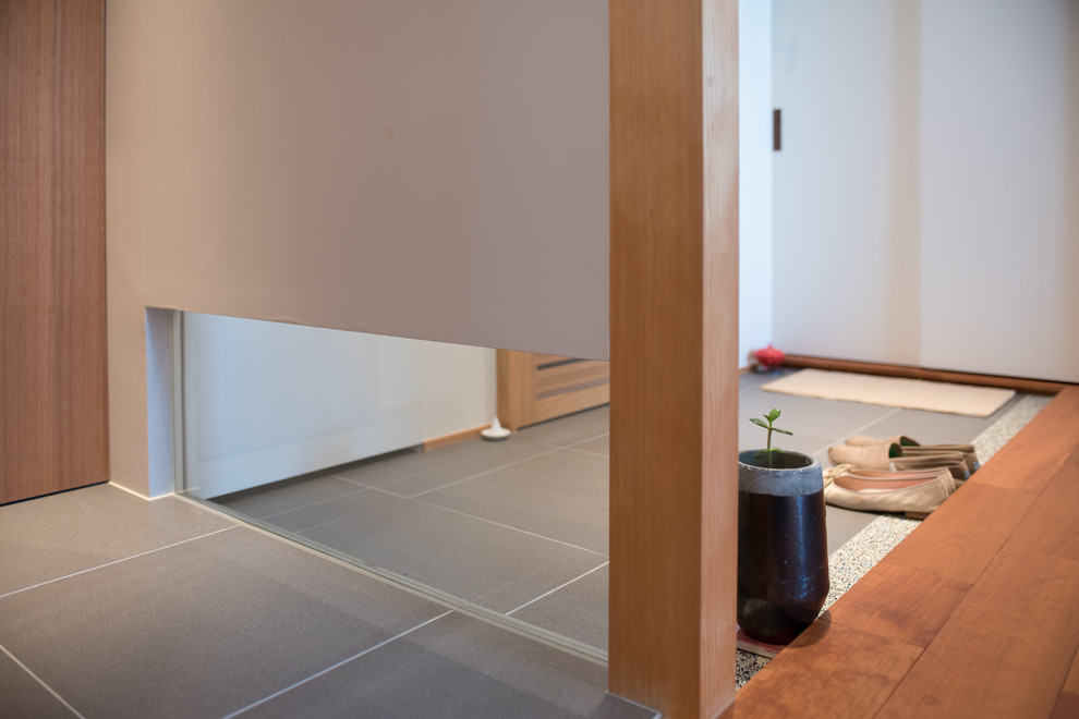 東京23区にある小さなコンテンポラリースタイルのおしゃれな玄関ロビー (白い壁、磁器タイルの床、淡色木目調のドア、グレーの床) の写真