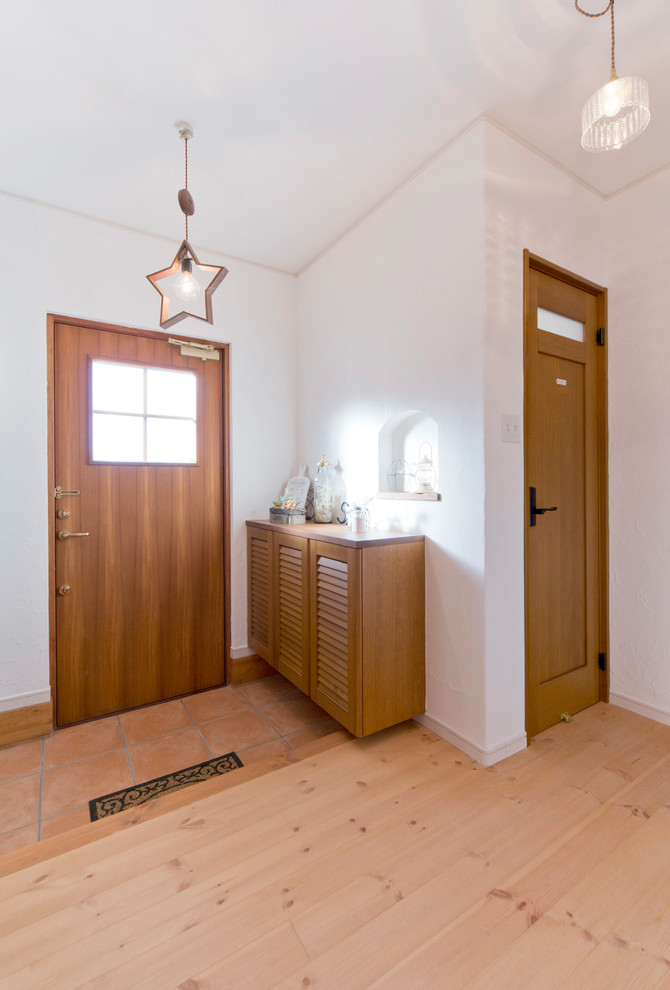 他の地域にあるカントリー風のおしゃれな玄関 (白い壁、テラコッタタイルの床、木目調のドア、オレンジの床) の写真