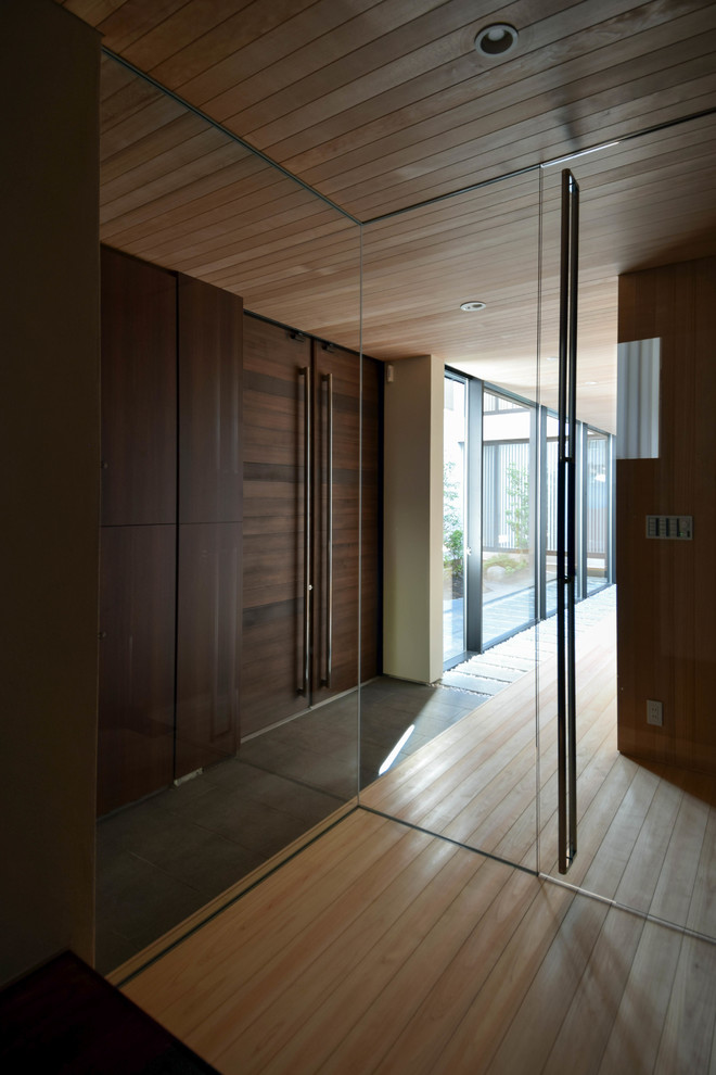 他の地域にある広いコンテンポラリースタイルのおしゃれな玄関 (茶色い壁、淡色無垢フローリング、濃色木目調のドア、ベージュの床) の写真