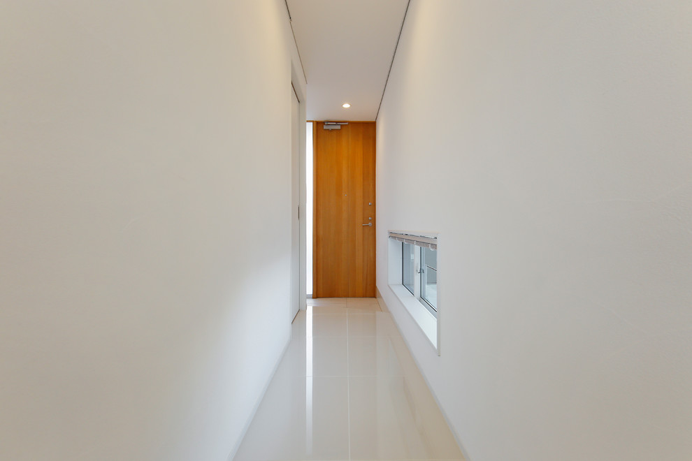 Ejemplo de hall moderno pequeño con paredes blancas, suelo de baldosas de cerámica, puerta simple, puerta de madera clara y suelo blanco