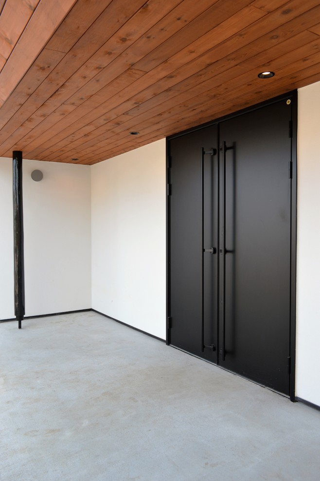 他の地域にあるモダンスタイルのおしゃれな玄関ドア (白い壁、コンクリートの床、黒いドア) の写真