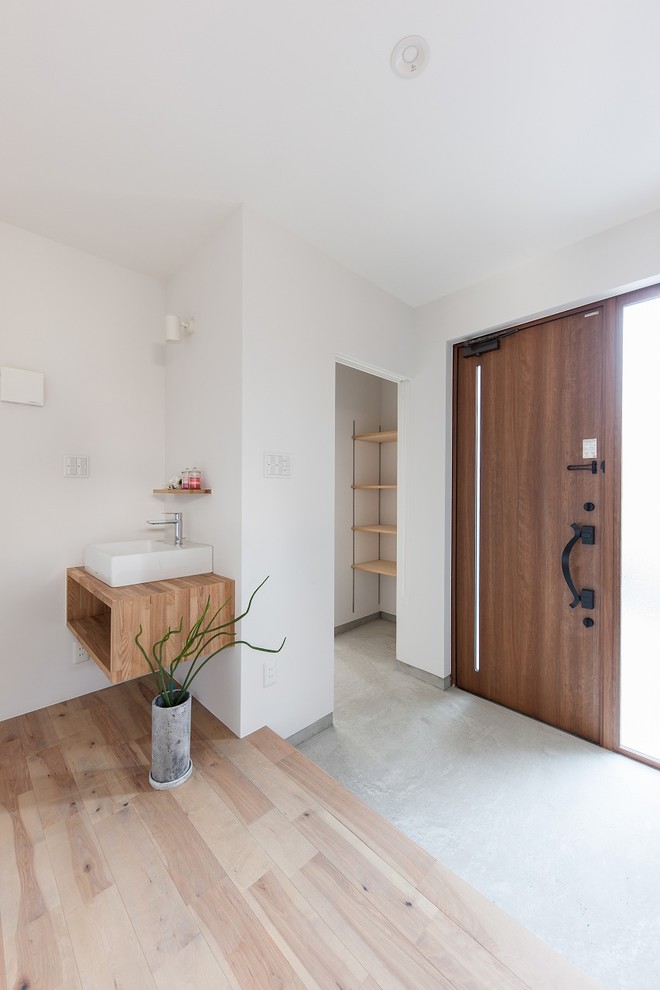 Ejemplo de hall de estilo zen con paredes blancas, suelo de cemento, puerta simple, puerta de madera en tonos medios y suelo gris